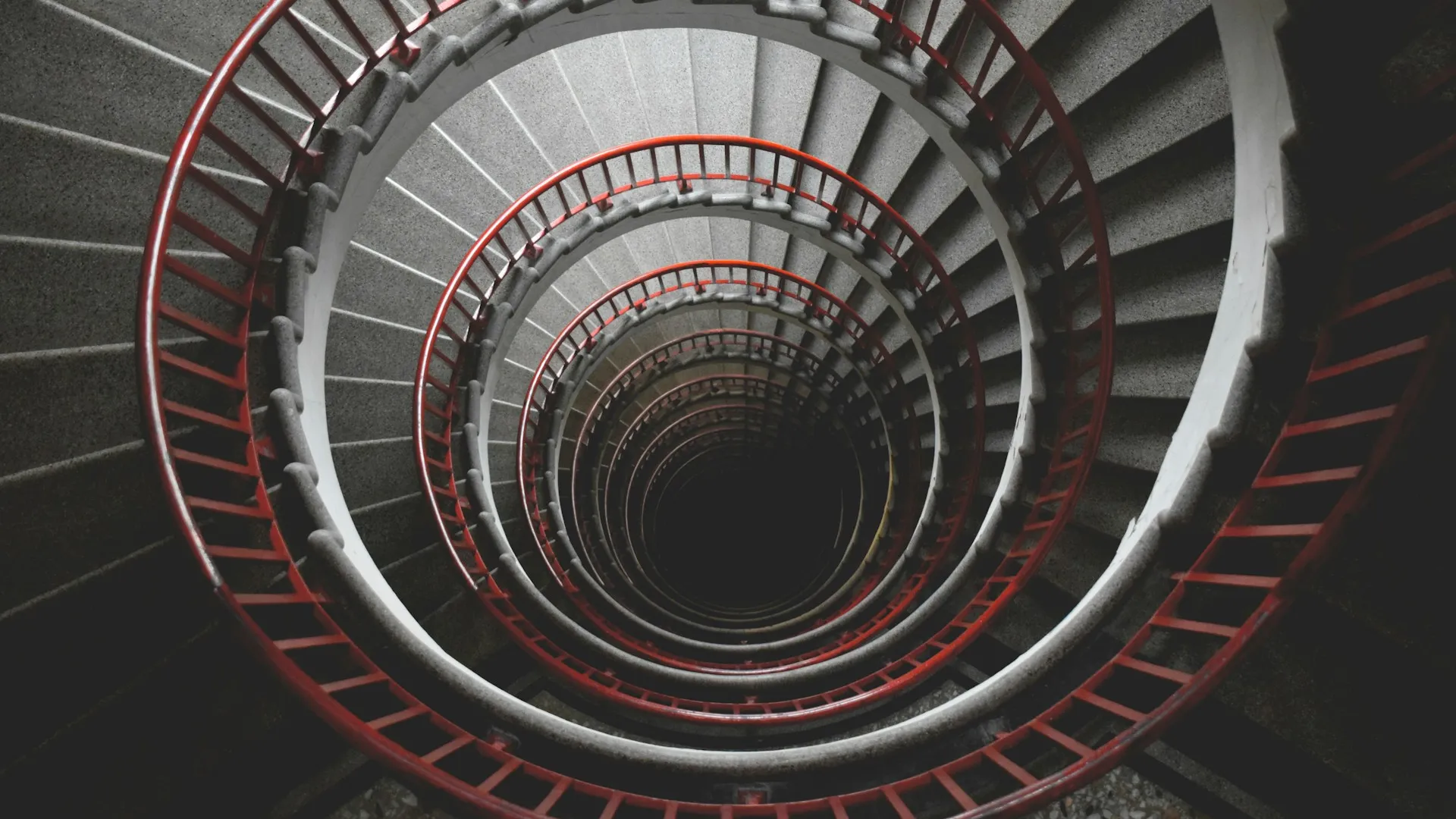 Spiral concrete staircase with a red fence seen from the top.