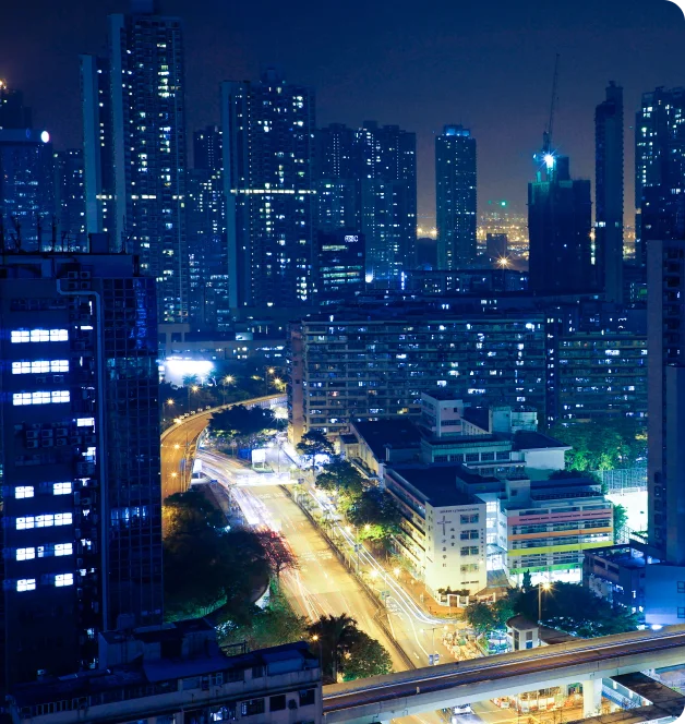 A city at night. A well lit road is running among tall sky scrapers.