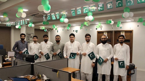A group of men holding small flags is standing under decorations for the Independence Day.