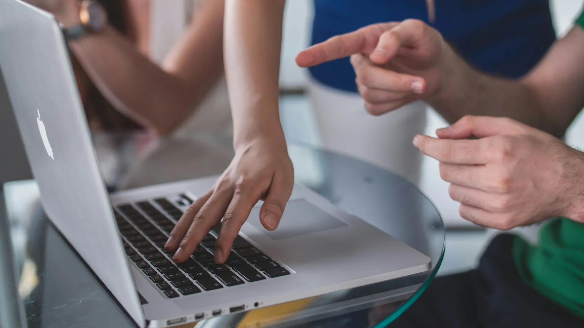 A human hand touching the kayboard of a laptop, and another pairof hands pointing at the laptop's screen.