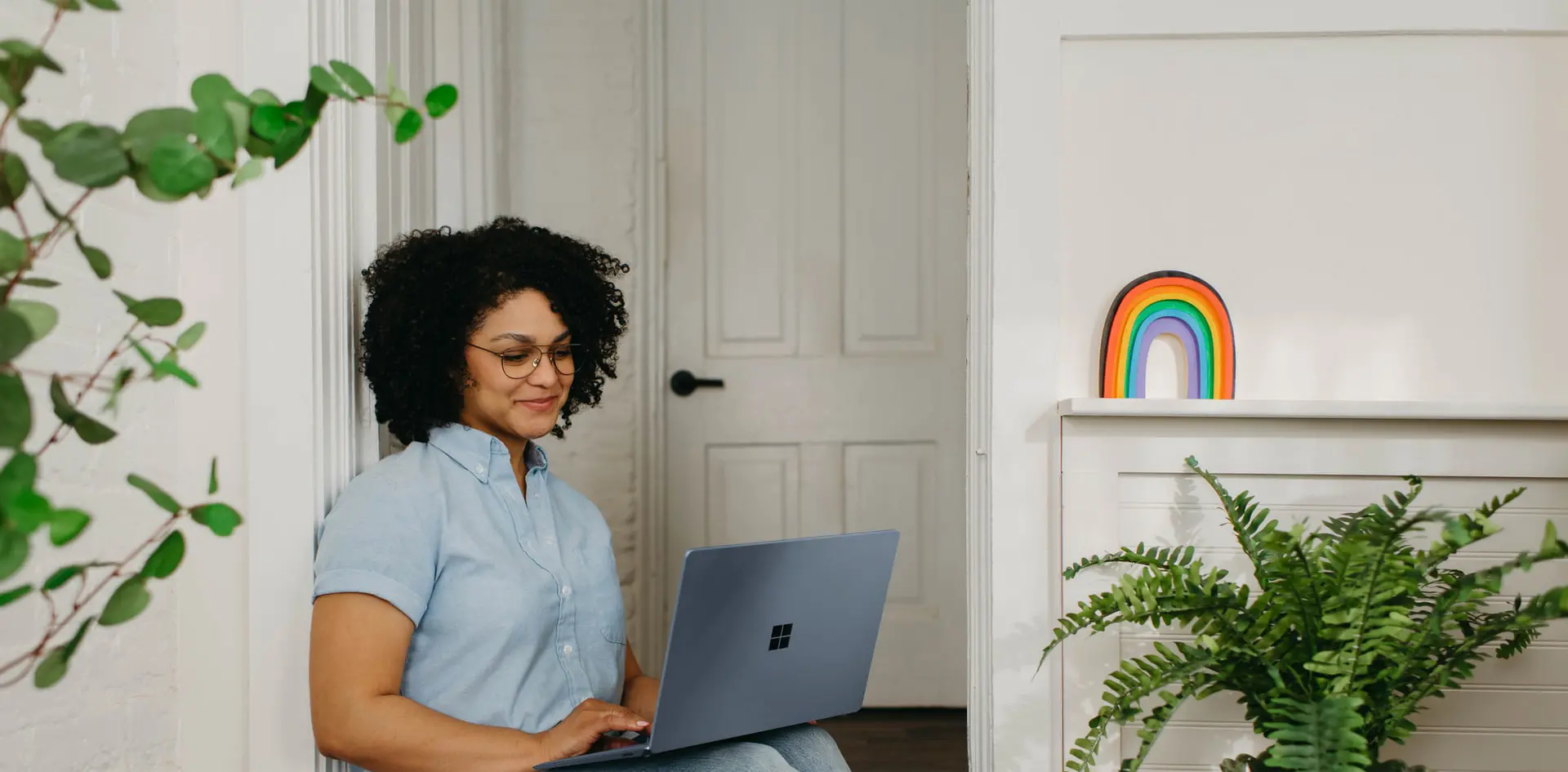 A student is sitting in a room with a laptop in her lap. She is smiling.