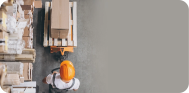 A warehouse worker (seen from the top) is pushing a cart with a pallet on top.